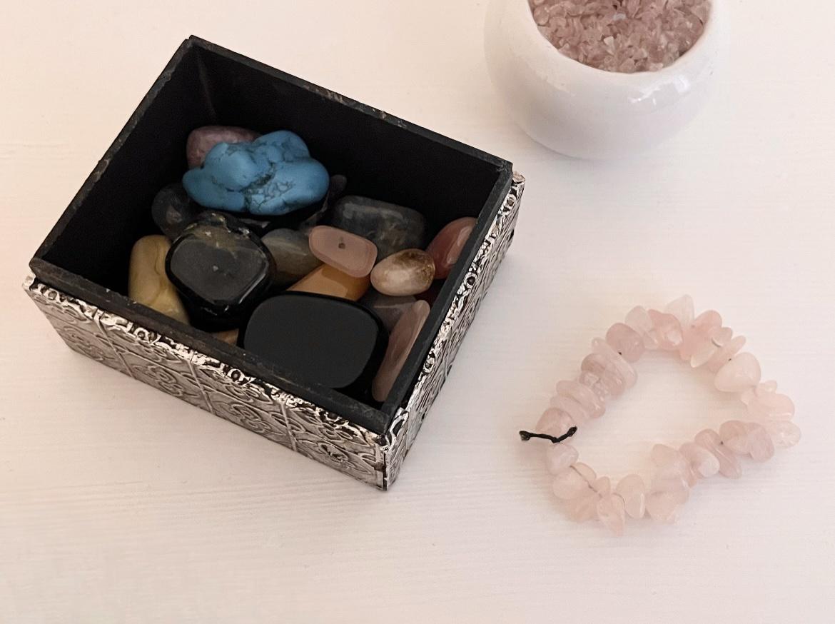 a box with different kinds of crystals in it and a bracelet made out of rose quartz beads